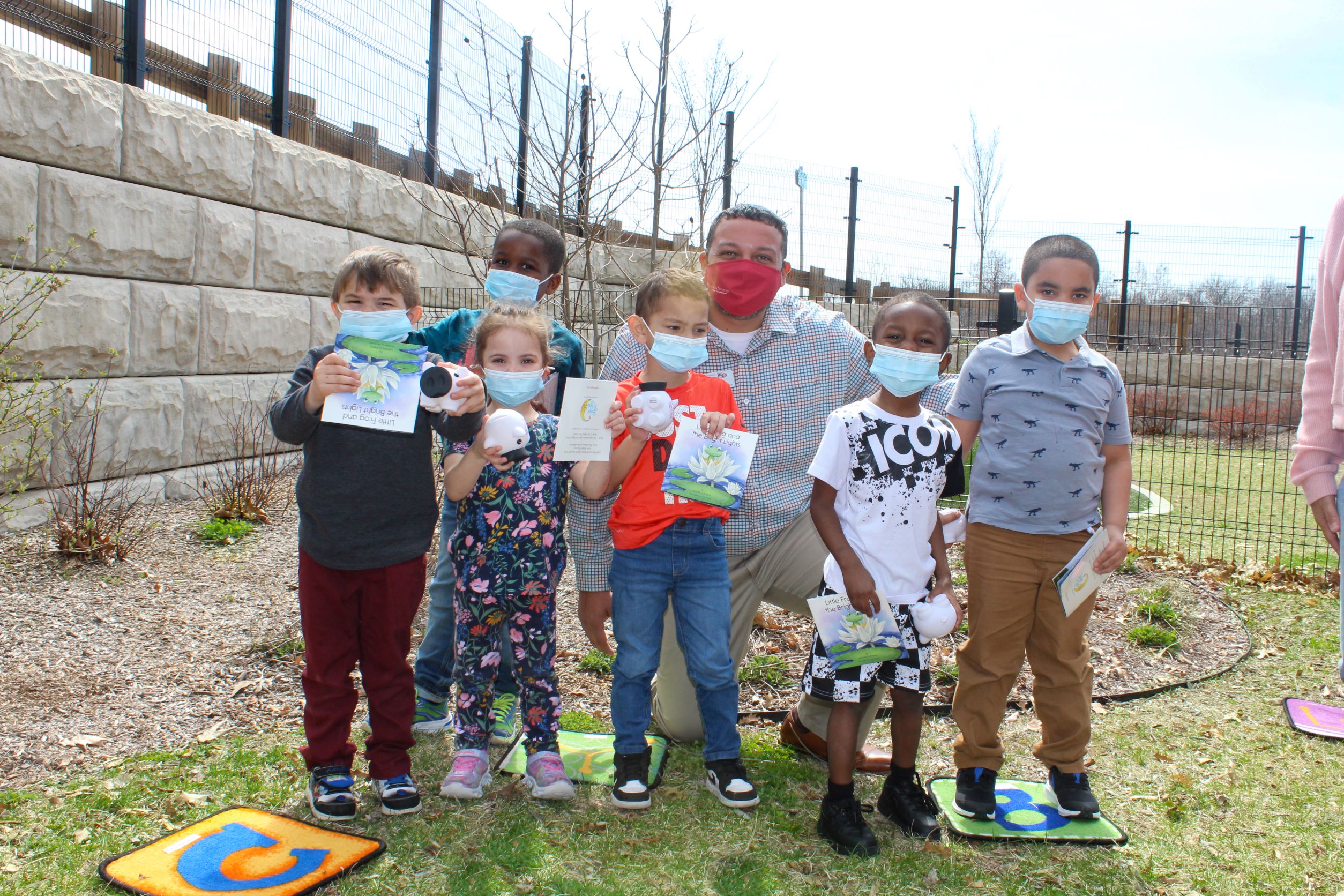 Wil Morales, Retail Banking & Security Officer and Monson Branch Manager of Monson Savings Bank, is shown smiling along with Educare Springfield preschool students holding their copy of the book “Little Frog and the Bright Lights” and their Monson Savings Bank piggy bank, following hearing the special story.